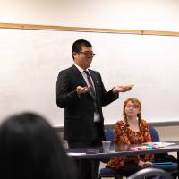Male student in a suit presenting in front of a conference room